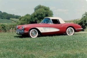 A vintage red convertible with a white top is parked on green grass.