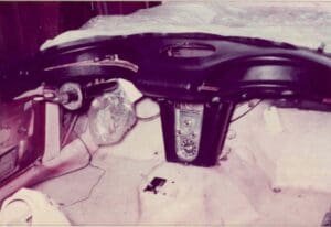 A vintage car interior without seats, exposing a retro dashboard with a central control panel and visible wiring, conveying a sense of nostalgia.