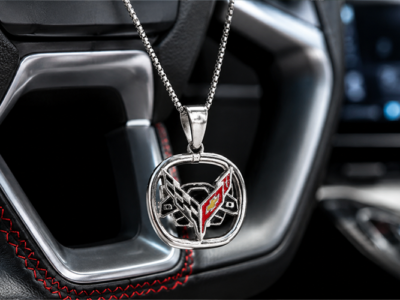Silver Corvette emblem pendant necklace hanging in front of a modern Corvette leather steering wheel with red stitching