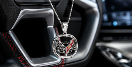 Silver Corvette emblem pendant necklace hanging in front of a modern Corvette leather steering wheel with red stitching