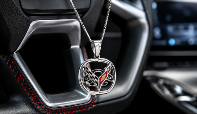 Silver Corvette emblem pendant necklace hanging in front of a modern Corvette leather steering wheel with red stitching